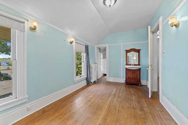 unfurnished bedroom with lofted ceiling, light wood-type flooring, radiator, and multiple windows