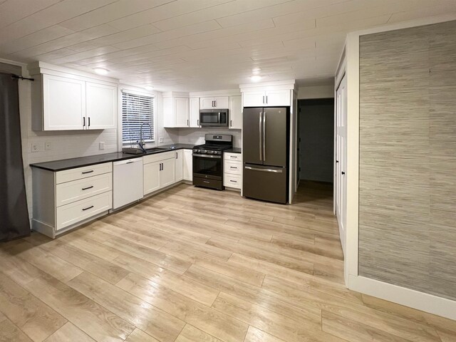 120 N Cedar St, Traverse City, MI 49684 - kitchen featuring stainless steel appliances, dark countertops, white cabinetry, light wood-type flooring, and a sink