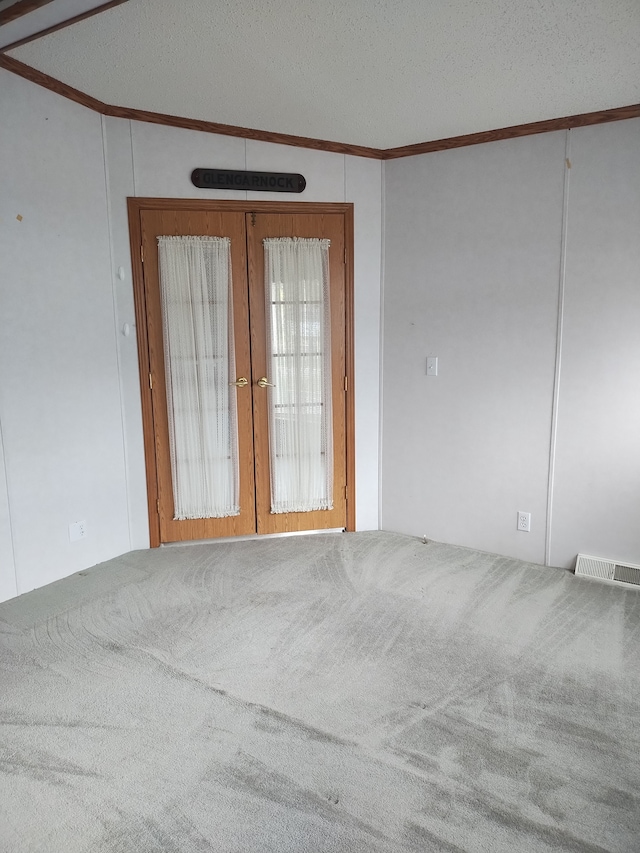 carpeted empty room with a textured ceiling, french doors, lofted ceiling, and ornamental molding