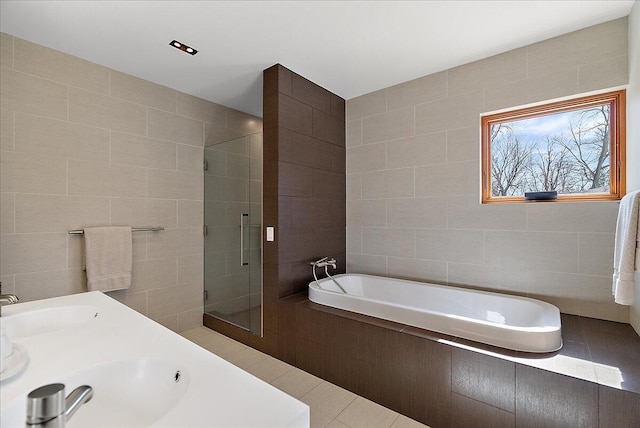 full bath featuring a bath, a shower stall, tile walls, and a sink