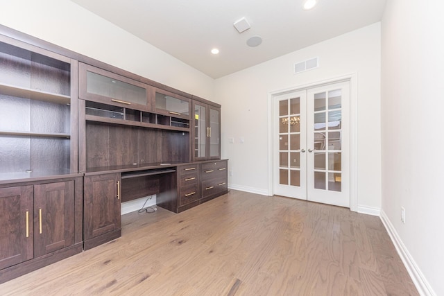 unfurnished office featuring french doors, built in desk, and light hardwood / wood-style flooring