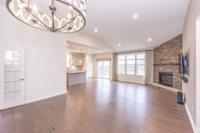 unfurnished living room with an inviting chandelier, lofted ceiling, a fireplace, and dark hardwood / wood-style flooring