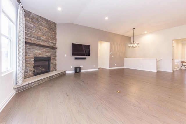 unfurnished living room featuring vaulted ceiling, a stone fireplace, hardwood / wood-style floors, and a chandelier