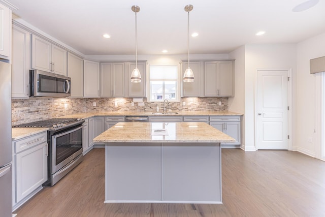 kitchen with sink, gray cabinets, appliances with stainless steel finishes, hanging light fixtures, and a kitchen island