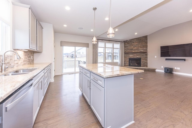 kitchen with sink, light stone counters, decorative light fixtures, stainless steel dishwasher, and a kitchen island