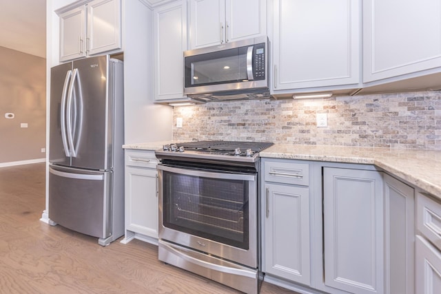 kitchen with light stone counters, tasteful backsplash, stainless steel appliances, and light hardwood / wood-style flooring