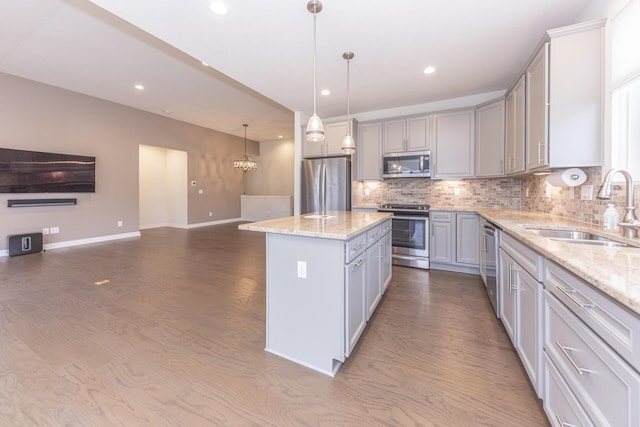 kitchen with sink, appliances with stainless steel finishes, a center island, light stone countertops, and decorative light fixtures