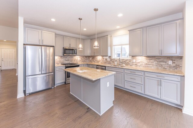 kitchen with sink, stainless steel appliances, a center island, light stone countertops, and decorative light fixtures