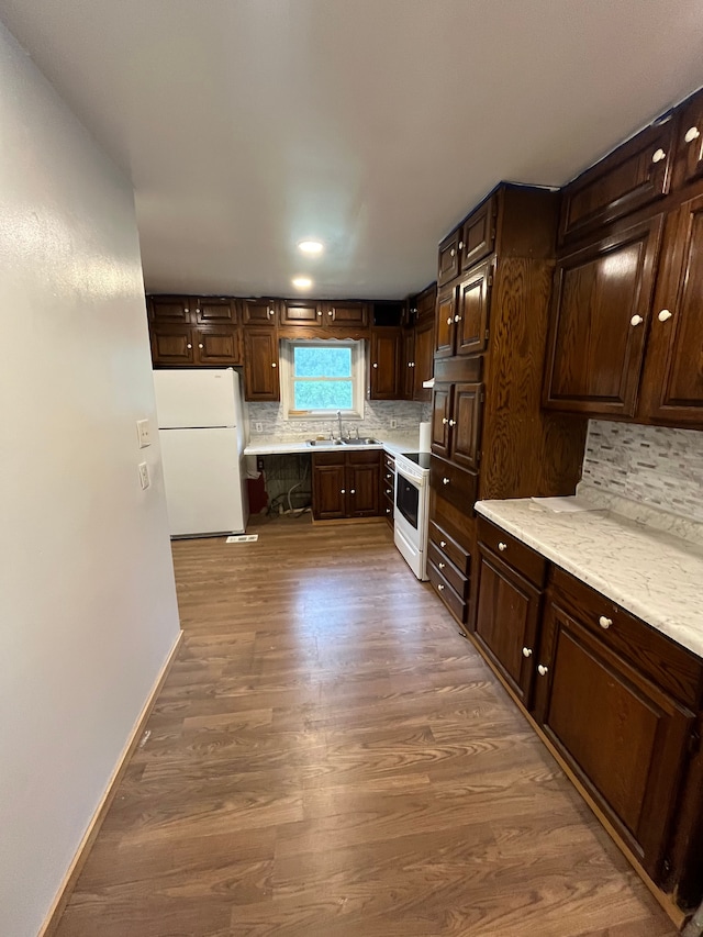 kitchen featuring decorative backsplash, dark brown cabinets, white appliances, sink, and dark hardwood / wood-style floors