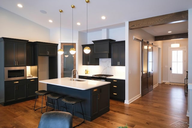 kitchen with pendant lighting, appliances with stainless steel finishes, an island with sink, decorative backsplash, and sink