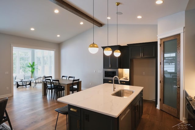 kitchen with decorative light fixtures, sink, light stone counters, and an island with sink