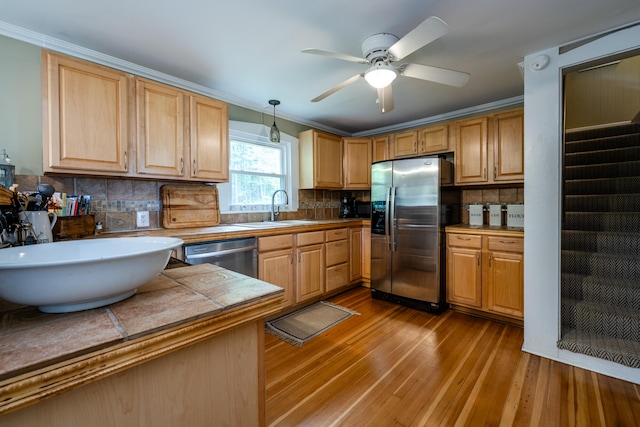 kitchen featuring sink, stainless steel appliances, tasteful backsplash, light hardwood / wood-style floors, and decorative light fixtures