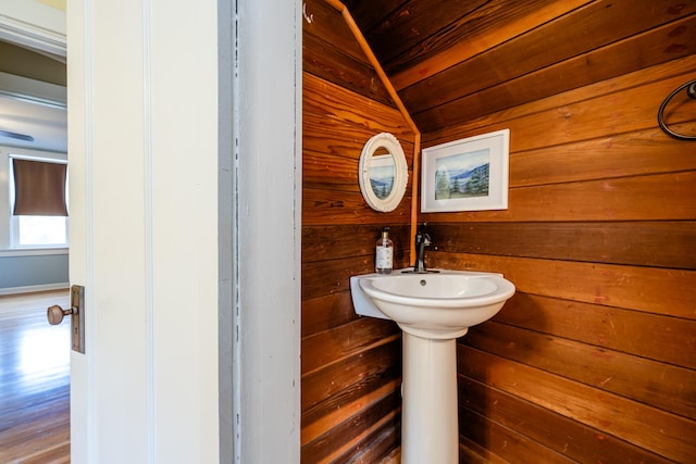 bathroom featuring wood-type flooring, vaulted ceiling, and wood walls