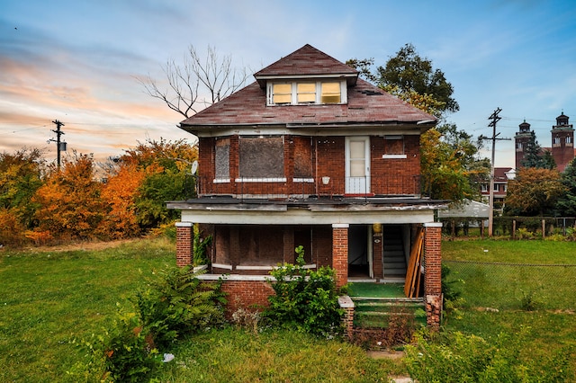 back house at dusk with a porch and a lawn