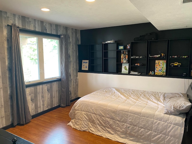 bedroom featuring wood walls, wood-type flooring, and a textured ceiling