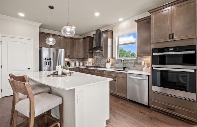 kitchen with a kitchen island, pendant lighting, sink, stainless steel appliances, and wall chimney exhaust hood