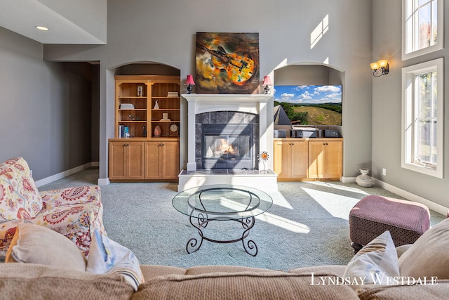 living room with a tiled fireplace, light carpet, and a high ceiling