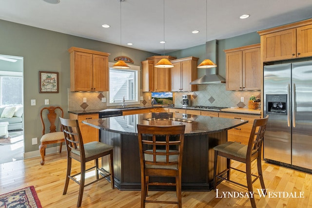 kitchen with a center island, wall chimney exhaust hood, a kitchen breakfast bar, pendant lighting, and appliances with stainless steel finishes