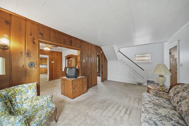 carpeted living room featuring ceiling fan, crown molding, and wooden walls