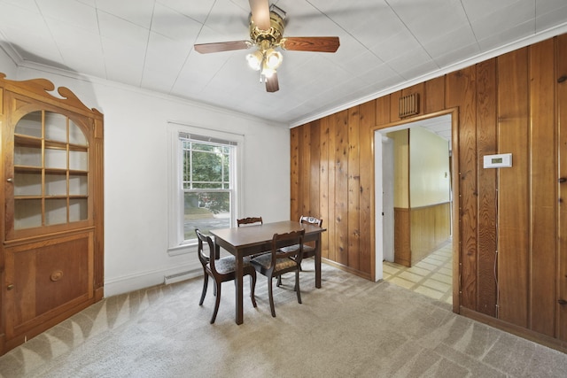 dining room with wood walls, ceiling fan, light carpet, and ornamental molding