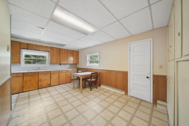 kitchen with wood walls, a drop ceiling, a baseboard radiator, and sink