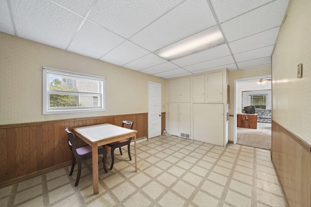 dining area featuring wood walls, a drop ceiling, and ceiling fan