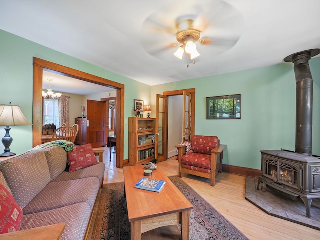 living room featuring ceiling fan with notable chandelier, light hardwood / wood-style floors, and a wood stove