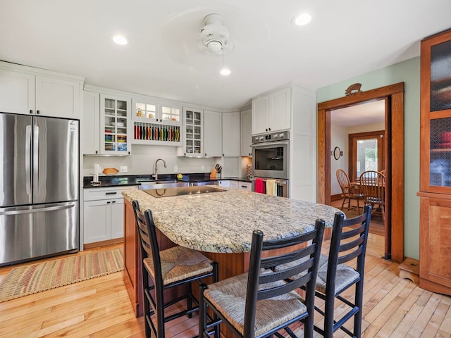 kitchen with ceiling fan, stainless steel appliances, a breakfast bar, white cabinets, and light wood-type flooring