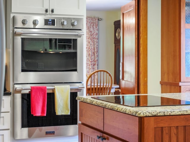 kitchen featuring white cabinets, black electric stovetop, light stone counters, and double oven