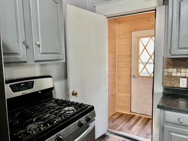 kitchen featuring tasteful backsplash, gray cabinetry, wooden walls, wood-type flooring, and stainless steel gas stove