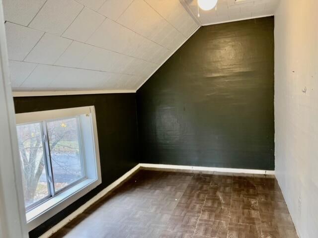 bonus room with dark parquet flooring and vaulted ceiling