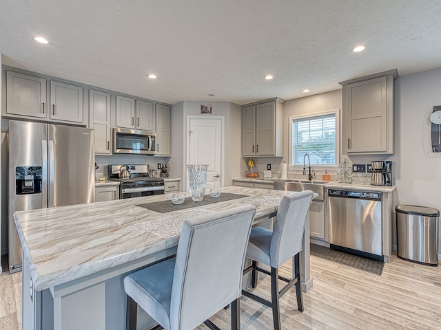 kitchen featuring gray cabinets, light wood-type flooring, a textured ceiling, appliances with stainless steel finishes, and a kitchen island