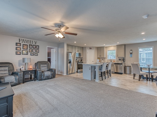 living room with ceiling fan, sink, light hardwood / wood-style floors, and a textured ceiling