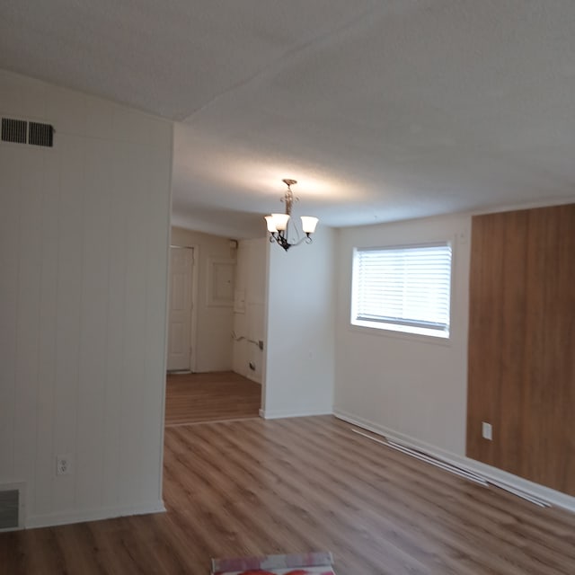 unfurnished room featuring wooden walls, an inviting chandelier, and hardwood / wood-style flooring