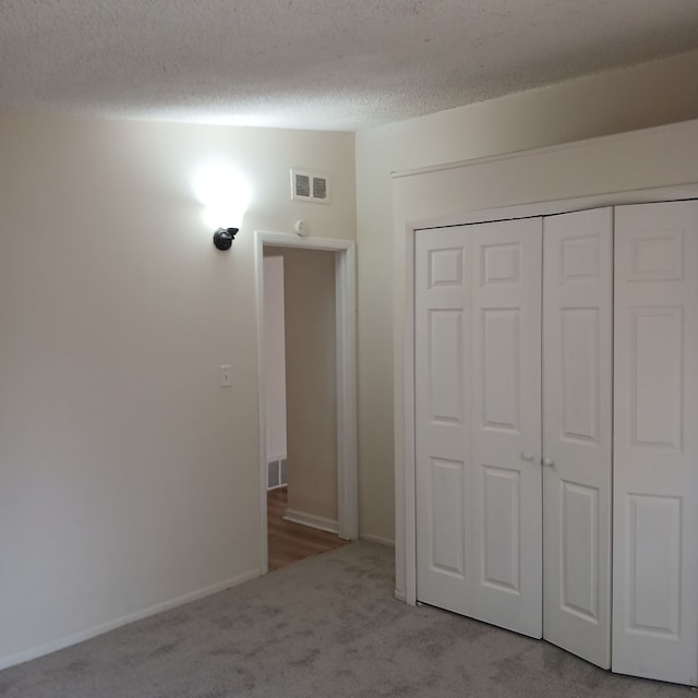 unfurnished bedroom featuring a textured ceiling, light carpet, and a closet