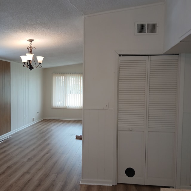 interior space featuring hardwood / wood-style floors, wood walls, an inviting chandelier, vaulted ceiling, and a textured ceiling