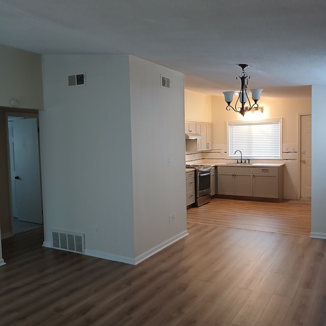 kitchen with sink, stainless steel range, an inviting chandelier, hardwood / wood-style floors, and decorative light fixtures