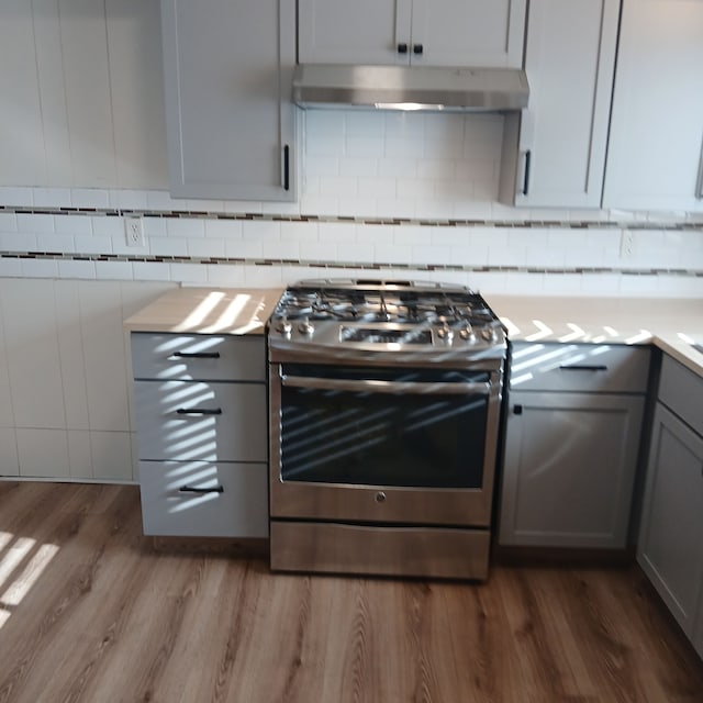 kitchen with exhaust hood, gas range, gray cabinets, tasteful backsplash, and dark hardwood / wood-style flooring