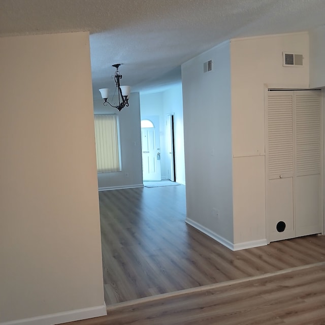 unfurnished room featuring wood-type flooring, a textured ceiling, and an inviting chandelier