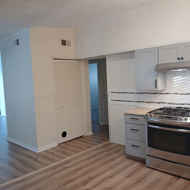 kitchen with gray cabinetry, stainless steel gas stove, tasteful backsplash, light hardwood / wood-style floors, and a textured ceiling