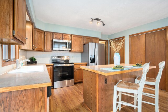 1875 Edwin Dr, Wayland, MI 49348 - kitchen with stainless steel appliances, brown cabinets, light wood-style floors, a kitchen bar, and a sink