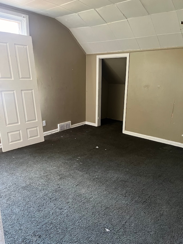 additional living space featuring dark carpet and vaulted ceiling