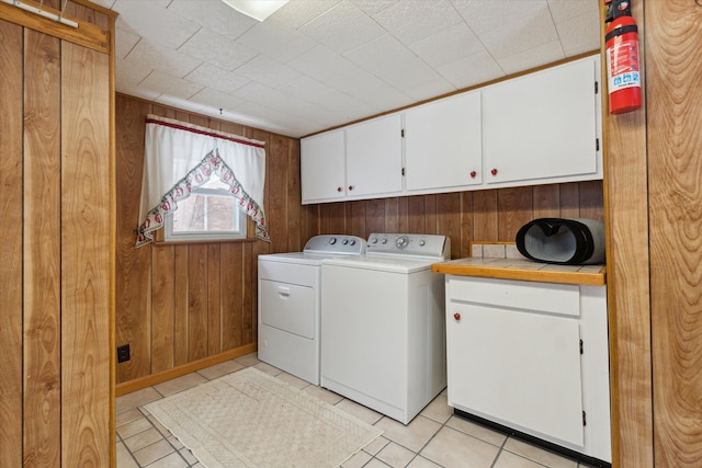 clothes washing area featuring cabinets, washing machine and dryer, light tile patterned floors, and wood walls