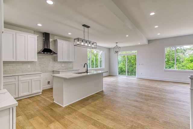 kitchen with light wood-type flooring, white cabinetry, a kitchen island with sink, and wall chimney exhaust hood