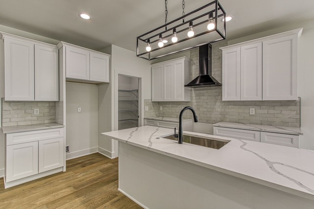 kitchen featuring white cabinets, pendant lighting, wall chimney range hood, and sink