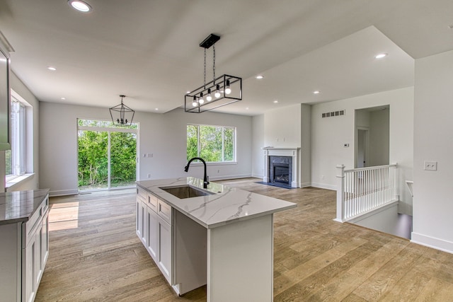 kitchen featuring sink, hanging light fixtures, light hardwood / wood-style flooring, light stone countertops, and an island with sink