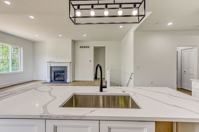 kitchen with light stone counters, sink, a fireplace, light hardwood / wood-style floors, and white cabinetry