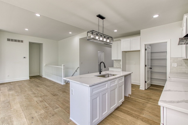 kitchen featuring backsplash, a center island with sink, white cabinets, sink, and light stone countertops