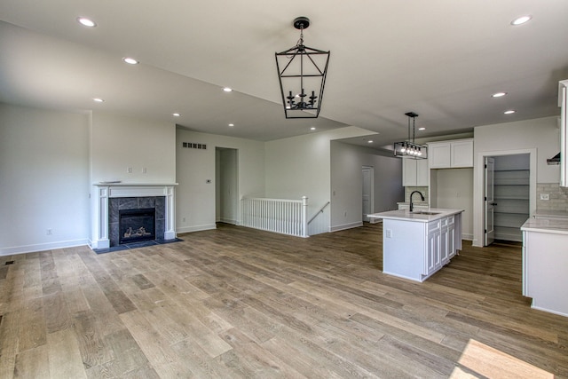 kitchen featuring white cabinetry, sink, hanging light fixtures, a tiled fireplace, and a kitchen island with sink