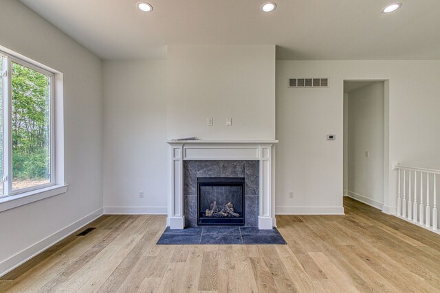 unfurnished living room with a tiled fireplace, a wealth of natural light, and light wood-type flooring